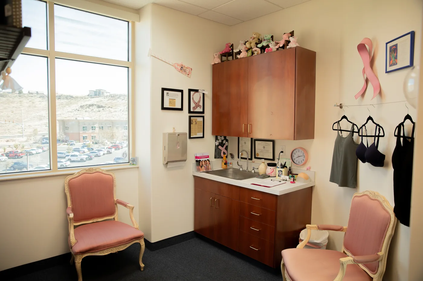 Carol's private fitting room — pink armchairs, a sunny window, and a wall of pink-ribbon keepsakes